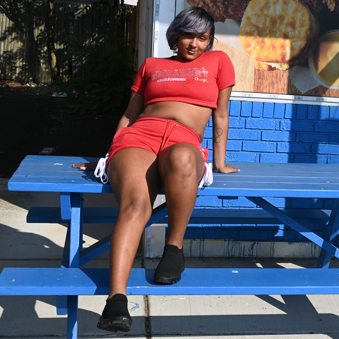 Person wearing a red outfit sitting on a blue picnic table with a blue wall and window in the background.