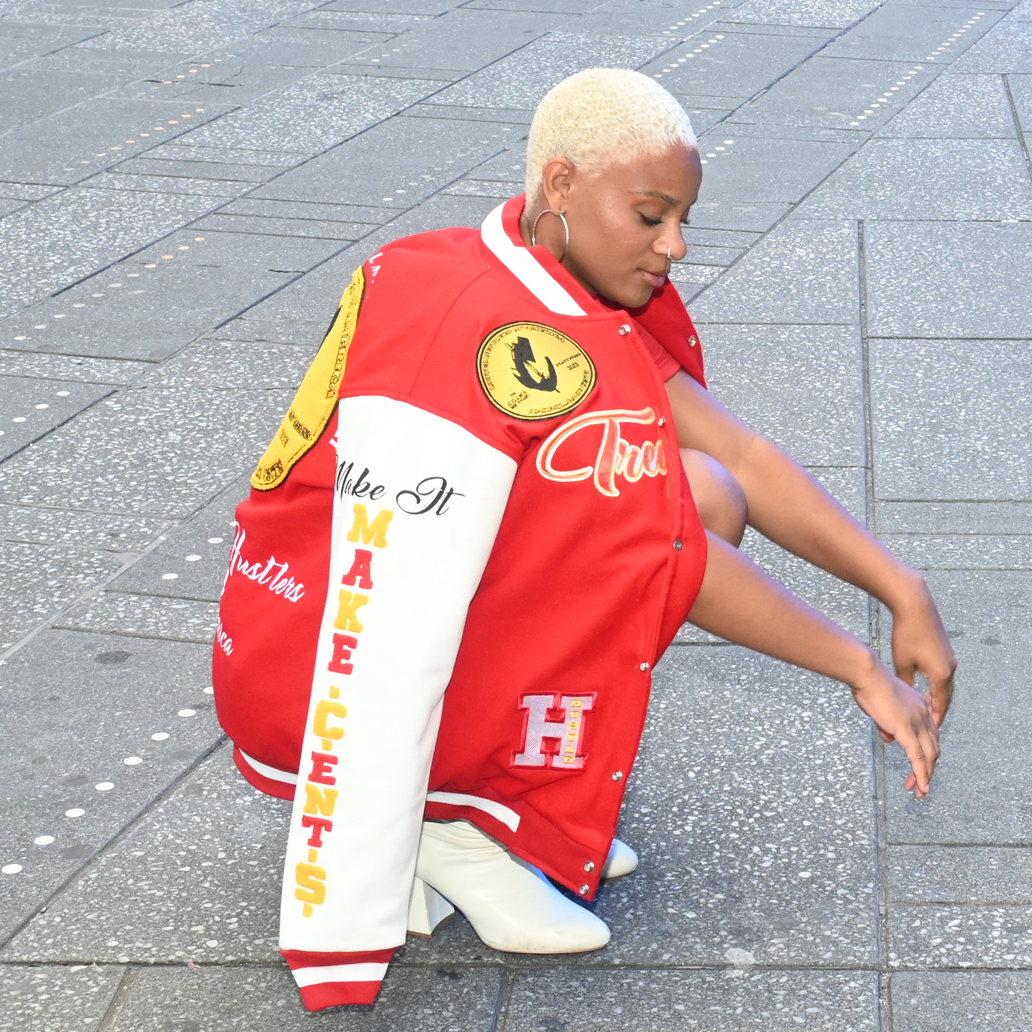 Person wearing a red varsity jacket with various patches on a paved ground