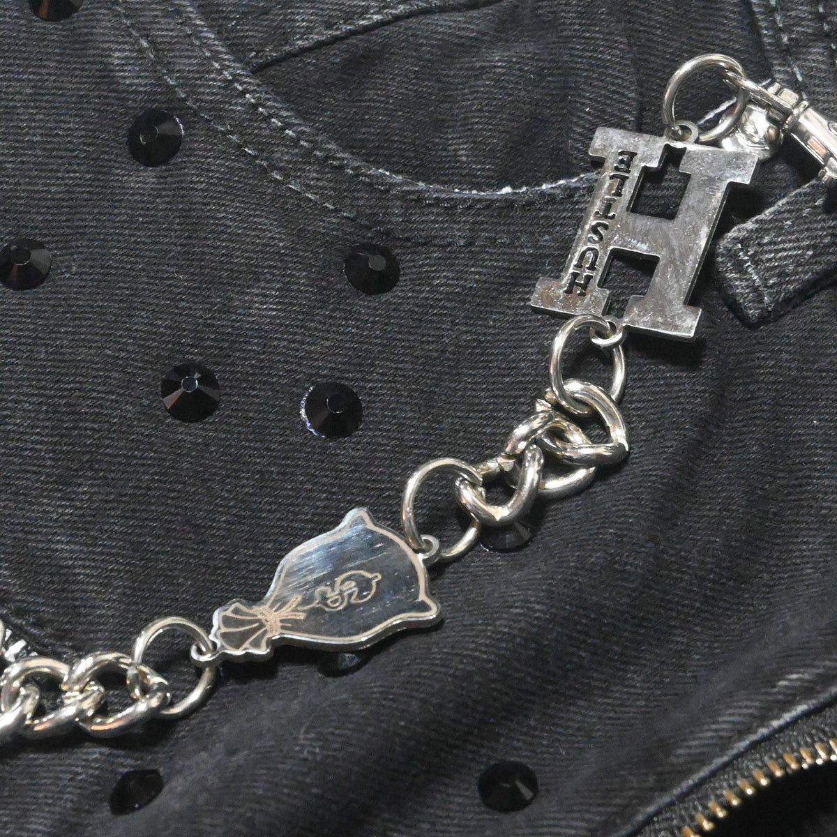 NUMMI VESTES black acid washed denim jeans featuring rhinestone studs, metallic chain, and Hustle H charm detail.
