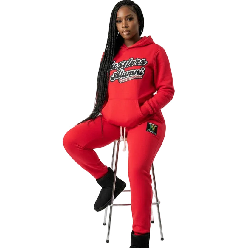 NUMMI VESTES red Hustlers Alumni cotton hooded sweatsuit worn by a woman sitting on a stool with black boots